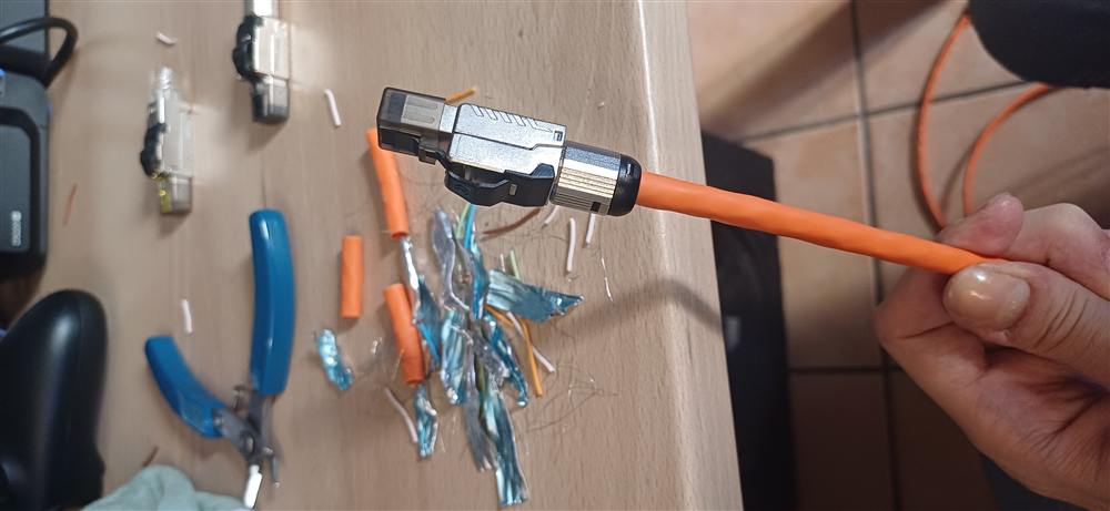 Sertissage d’un connecteur RJ45 blindé sur un câble réseau orange, pince et chutes de câble sur l’établi.